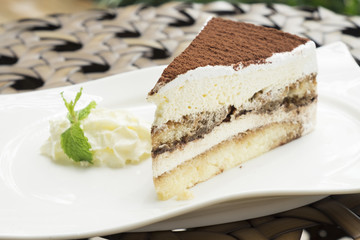 tiramisu cake served with whipped cream in the white dish
