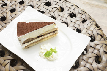 tiramisu cake served with whipped cream in the white dish