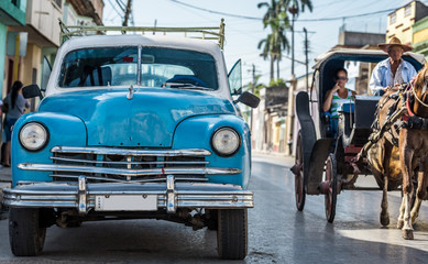 Blauer amerikanischer Oldtimer parkt neben einer Kutsche auf der Strasse 