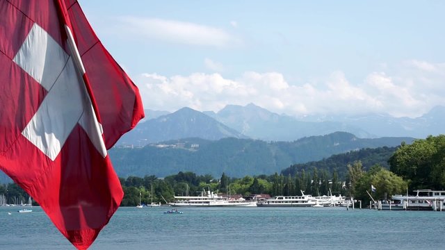Panorama view the of lake lucerne in switzerland with huge swiss flag waving in the foreground.