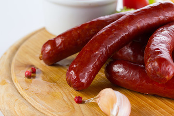 Tasty grilled sausages with vegetables and sauce close up on wooden board isolated on white background