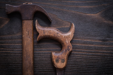 Rusted messy handsaw and claw hammer on vintage wooden backgroun