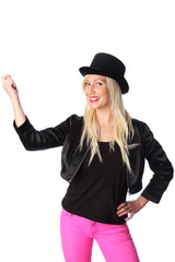 Attractive blonde woman in her 20s wearing a black jacket, pink pants and a top hat. White background.