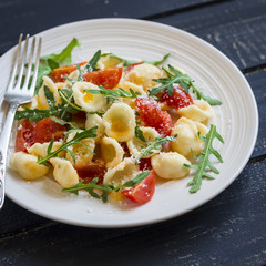 orecchiette pasta with tomatoes, Parmesan and rocket salad on a plate light on a dark wooden background