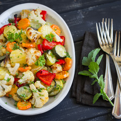 roasted vegetables - zucchini, cauliflower, potatoes, carrots, onions, peppers, on an oval dish on dark wooden background