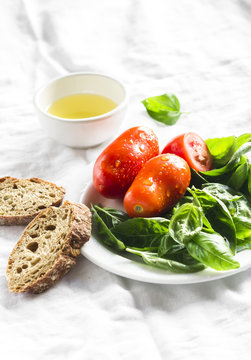 fresh Basil, tomatoes on a white plate, olive oil and a baguette on a white surface