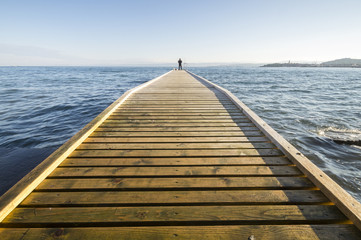 Postać wędkarza na końcu drewnianego pomostu wychodzącego w morze © Mike Mareen