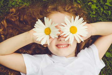 Child with daisy eyes, on green grass in a summer park.