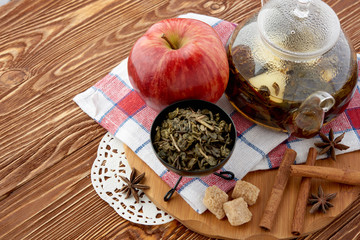Ripe apple, cinnamon and fruit drink in glass teapot on wooden