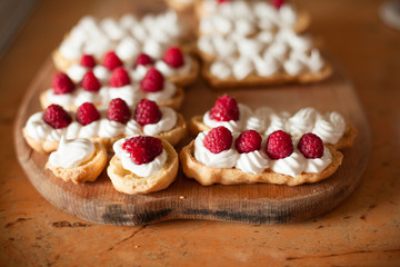 Cream eclairs with fresh raspberries on wood table