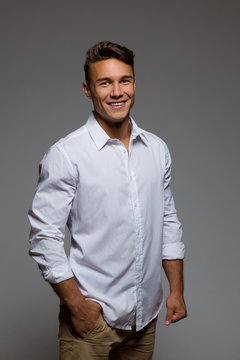 Young handsome man in white shirt posing with hand in pocket. Three quarter length studio shot on gray background.