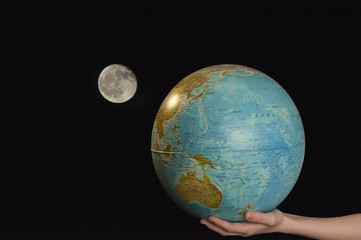 Earth and moon/Child's hand holding a globe against the background of dark sky with the moon

