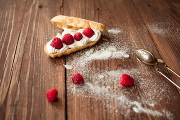 Eclair with fresh raspberries on wood table, confectioner table