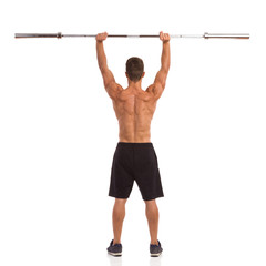 Muscular man holding a barbell over his head. Rear view. Full length studio shot isolated on white.