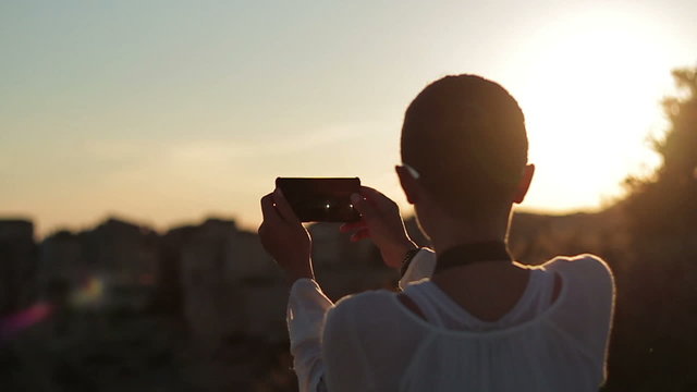 Young woman uses a smartphone to video a beautiful view at sunset, slow motion