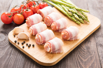 Bacon rolls with tomato, garlic, asparagus on wooden background