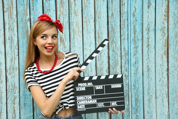 Obraz premium Beautiful girl with pretty smile holding clapboard on color wooden background