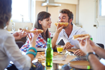 Two couples eating pizza, girl feeding guy with piece of pizza