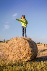 Naklejka na ściany i meble Happy baby girl sitting on a haystack in a field