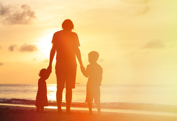 father and two kids walking on sunset beach