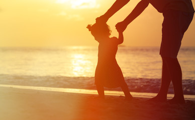 silhouettes of father and little daughter walking  at sunset