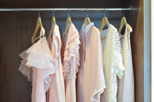 Sweet pastel blouses are hanging in open wooden wardrobe