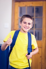 Smiling pupil with schoolbag doing thumbs up in a classroom