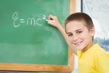 Smiling pupil writing on chalkboard in a classroom