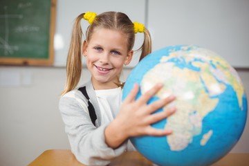 Cute pupil holding globe in a classroom