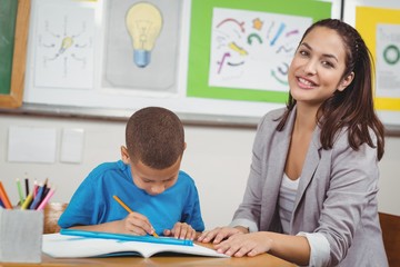 Obraz premium Pretty teacher helping pupil at his desk 