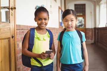 Cute pupils with smartphone at corridor