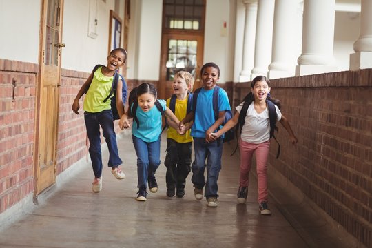 Happy pupils holding hands and running at corridor