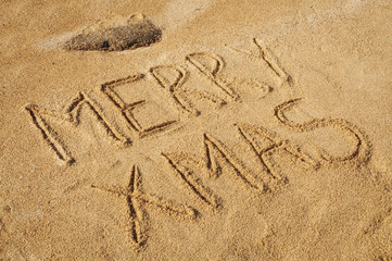 The words Merry Xmas written in the sand on the beach
