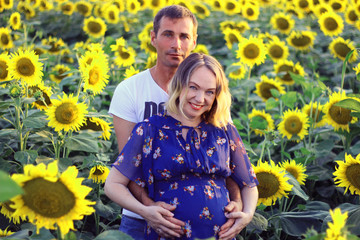 Happy couple - Husband and his pregnant wife in a field of sunflowers