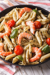 penne pasta with shrimp, tomato and pesto on a plate closeup. vertical
