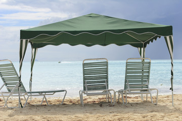 Empty beach chairs on under canopy with persona watercraft in the distance.