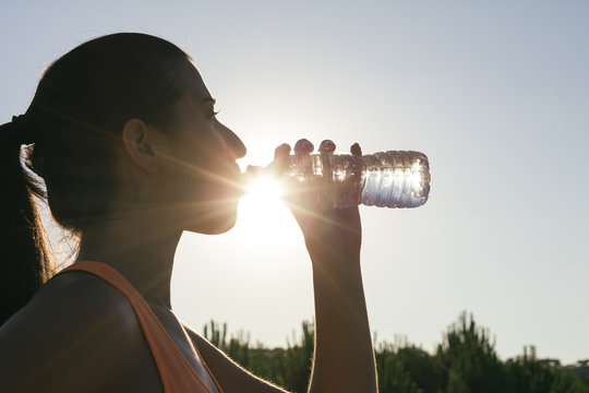 Backlighting of a runner woman drinking water