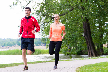 Woman and man jogging on dirt path in the woods together