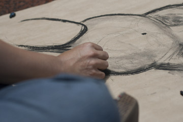 Artist painting with charcoal a pregnant woman on brown paper sitting on the floor.