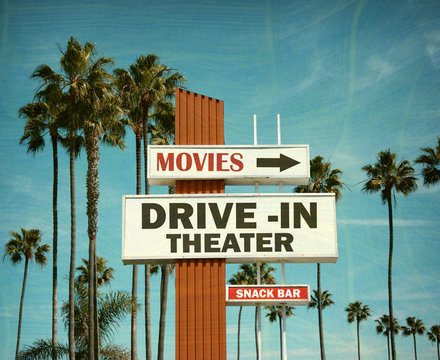 aged and worn vintage photo of drive in theater sign with pal trees