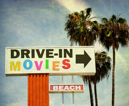 aged and worn vintage photo of retro drive in movies sign with palm trees