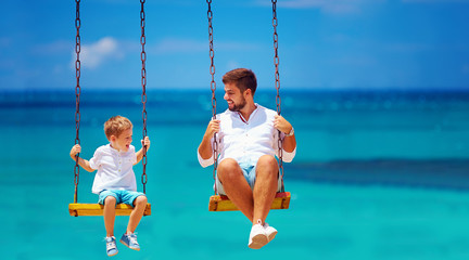 joyful father and son having fun on swings, sea background