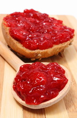 Strawberry jam on wooden spoon and whole wheat bread