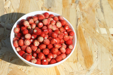 Ripe red wild strawberry in a plate on a wooden table outdoors