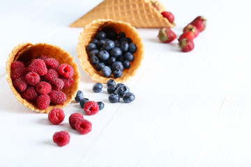Waffle cones with berries on wooden table