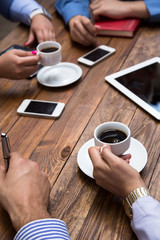 Informal business meeting Wooden cafe desk and hands of people drinking coffee with many electronic devices business style dress code male and female telephones tablets PC
