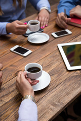 Coffee break Business people drinking coffee at wooden plank table modern electronic gadgets dropped around