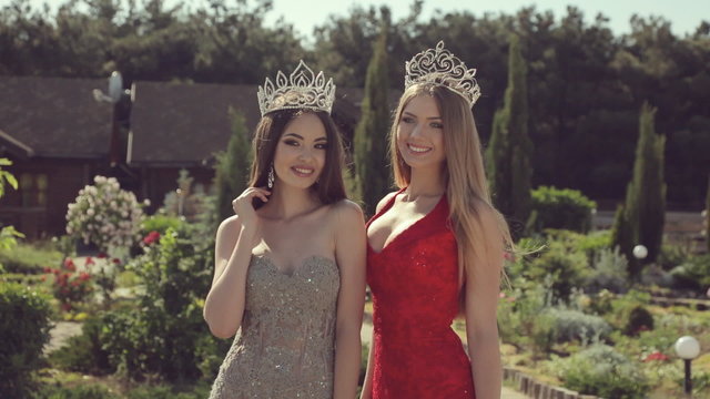 Two sexy young girls in evening gowns and crowns smiling and