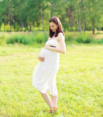Beautiful happy young smiling pregnant woman in white dress outd