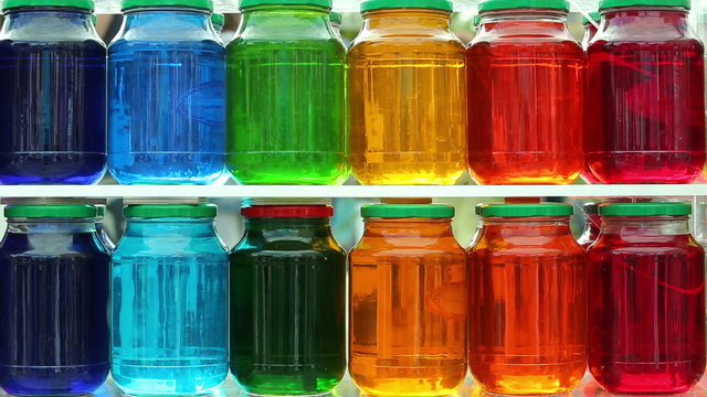 Lots of glass jars with colorful fruit compote in the window of a grocery store.